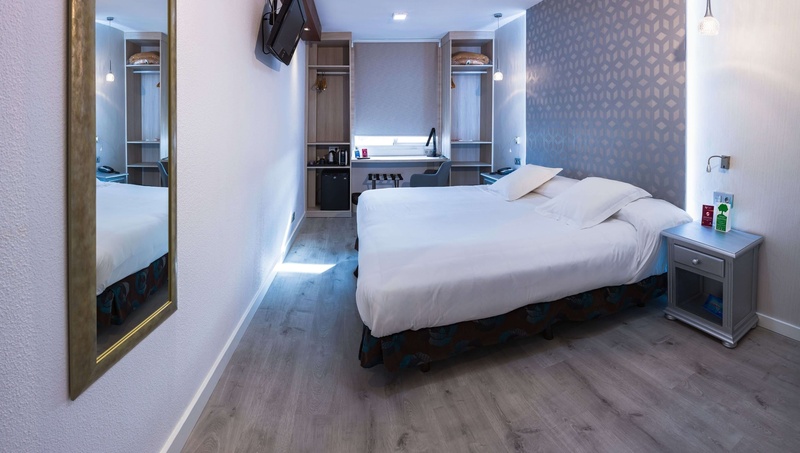 La foto mostra una moderna camera d'albergo ben arredata con un letto, un'area scrivania e armadi aperti, illuminata da luce artificiale.