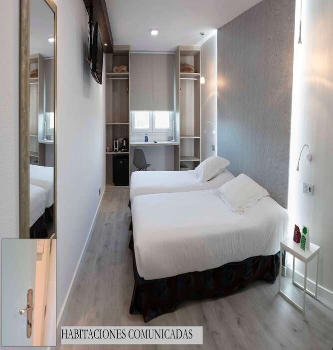 Una moderna camera d'albergo è arredata con due letti singoli, una scrivania con sedia e finestra, un armadio integrato con mini-frigo e TV a parete, e decorata con carta da parati testurizzata.