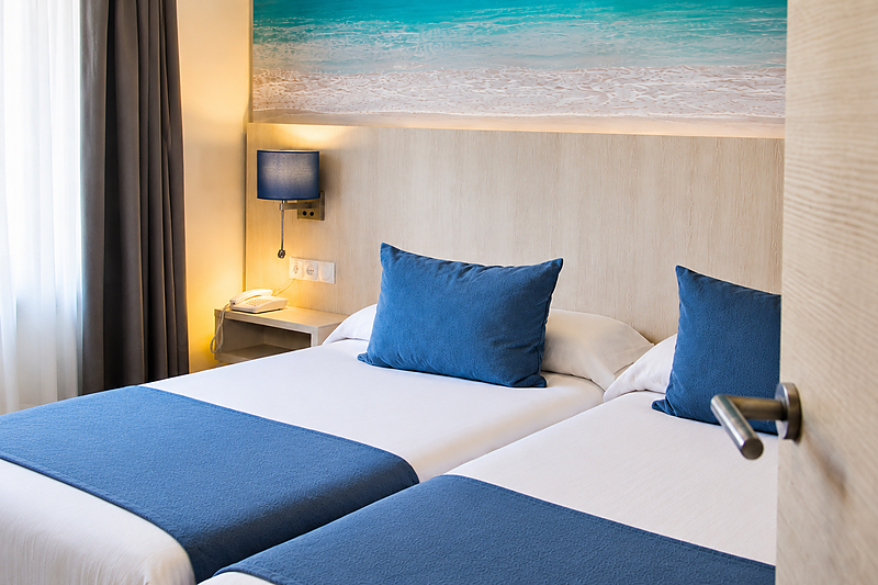 Twee witte bedden met blauwe plaids en kussens in een kamer van het Benalmádena Palace