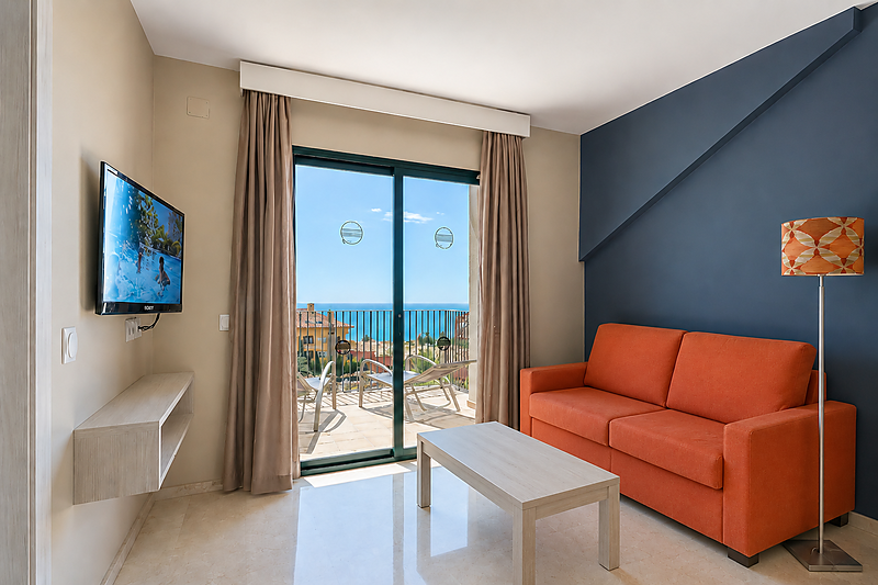 Lichte woonkamer met oranje bank, tv en balkon met zeezicht in het Benalmádena Palace