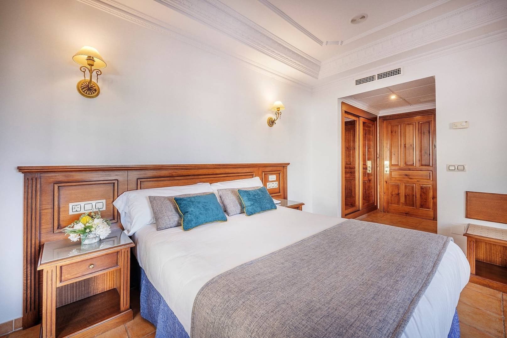 Habitación con cama doble, mesita de noche, flores y armario de madera. BENESTE: Corporativa.