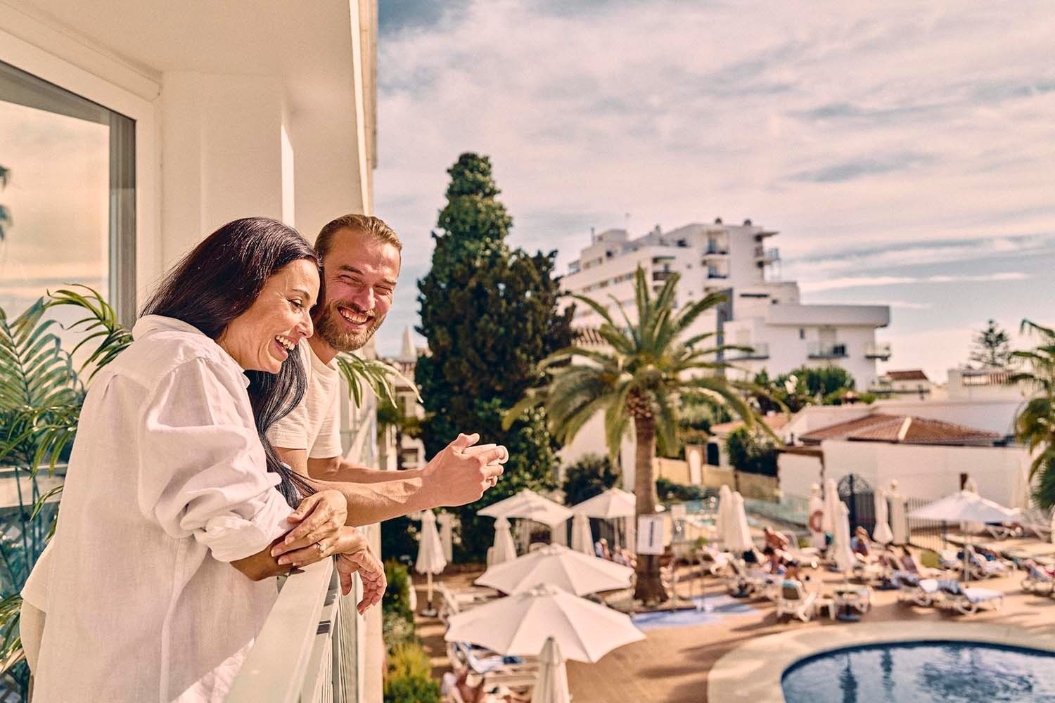 Pareja sonriendo en balcón con vistas a la piscina. Villa Flamenca | Beneste Hoteles.