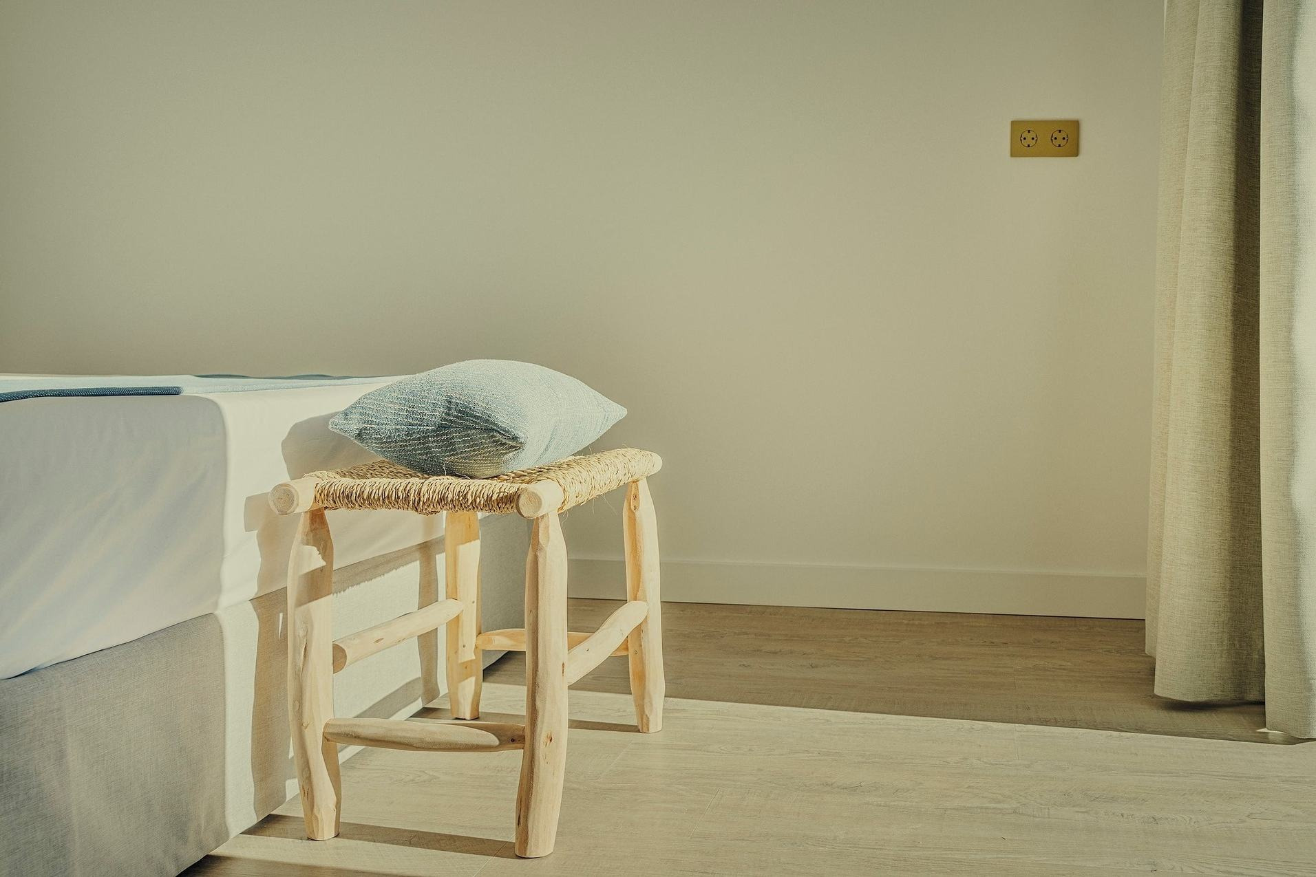 BENESTE: Silla rústica y almohada junto a la cama, luz cálida.