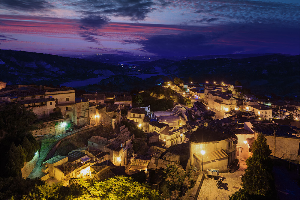 Vista nocturna de un pueblo italiano con casas iluminadas, ideal para un @BENESTE: Corporativa relajante.