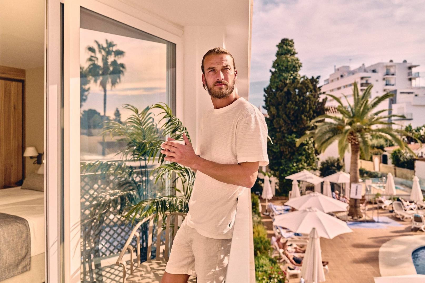 Villa Flamenca | Beneste Hoteles: Hombre en balcón con café, vistas a piscina y palmeras.