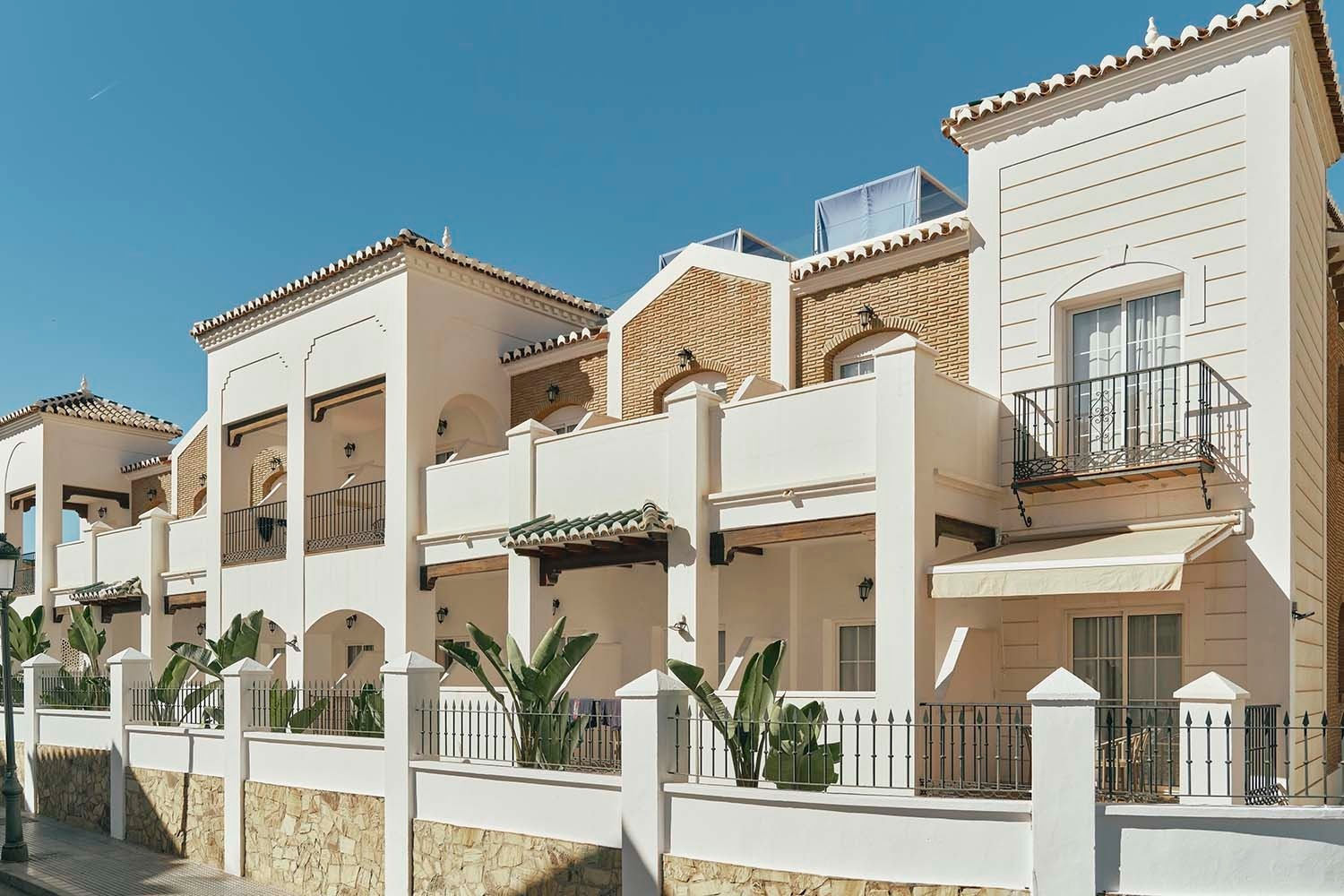Villa Flamenca: exteriores de hotel blanco con balcones y plantas tropicales. Web oficial.