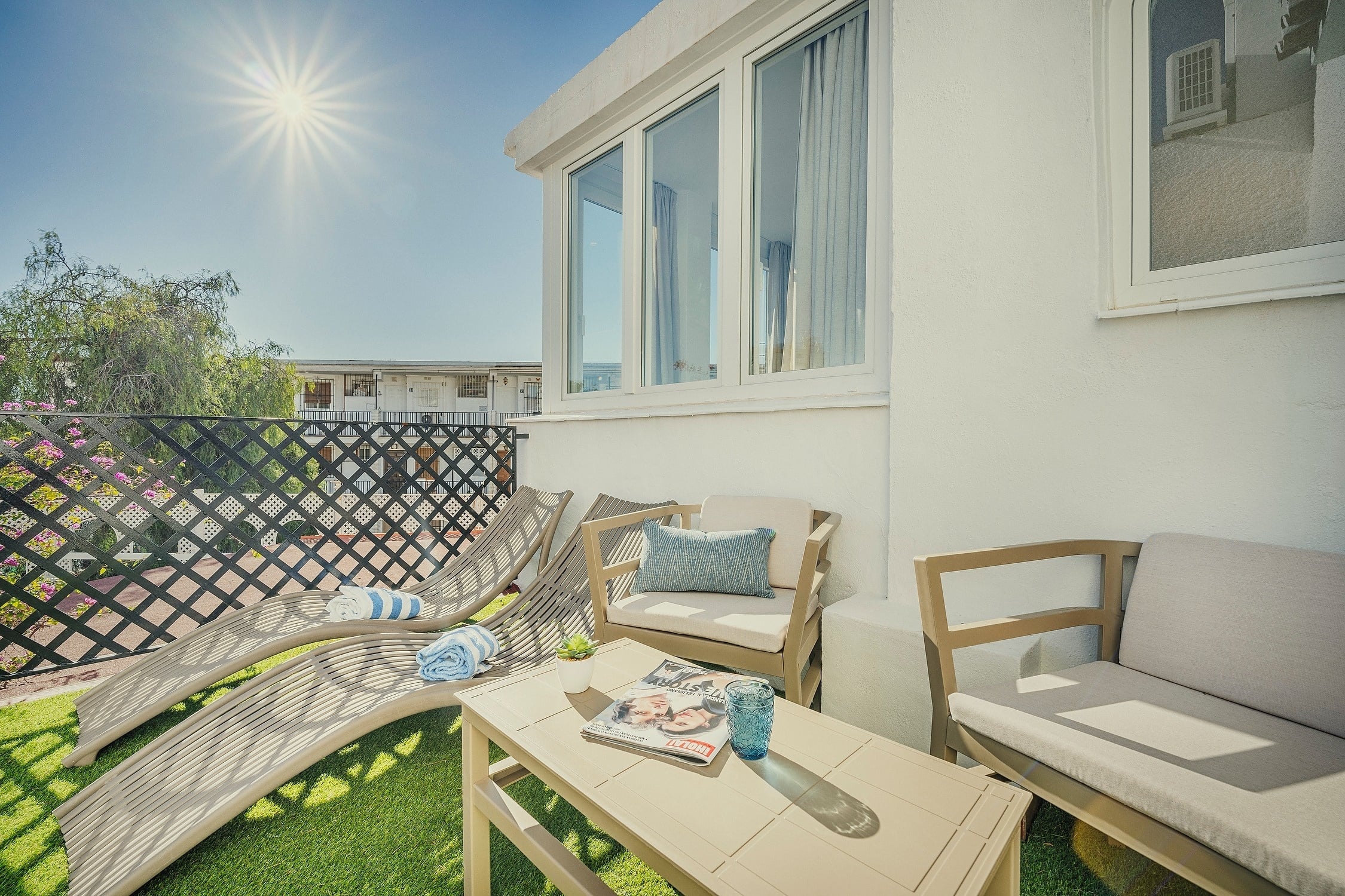 Un patio exterior soleado con césped artificial y cómodos muebles, ideal para la relajación.