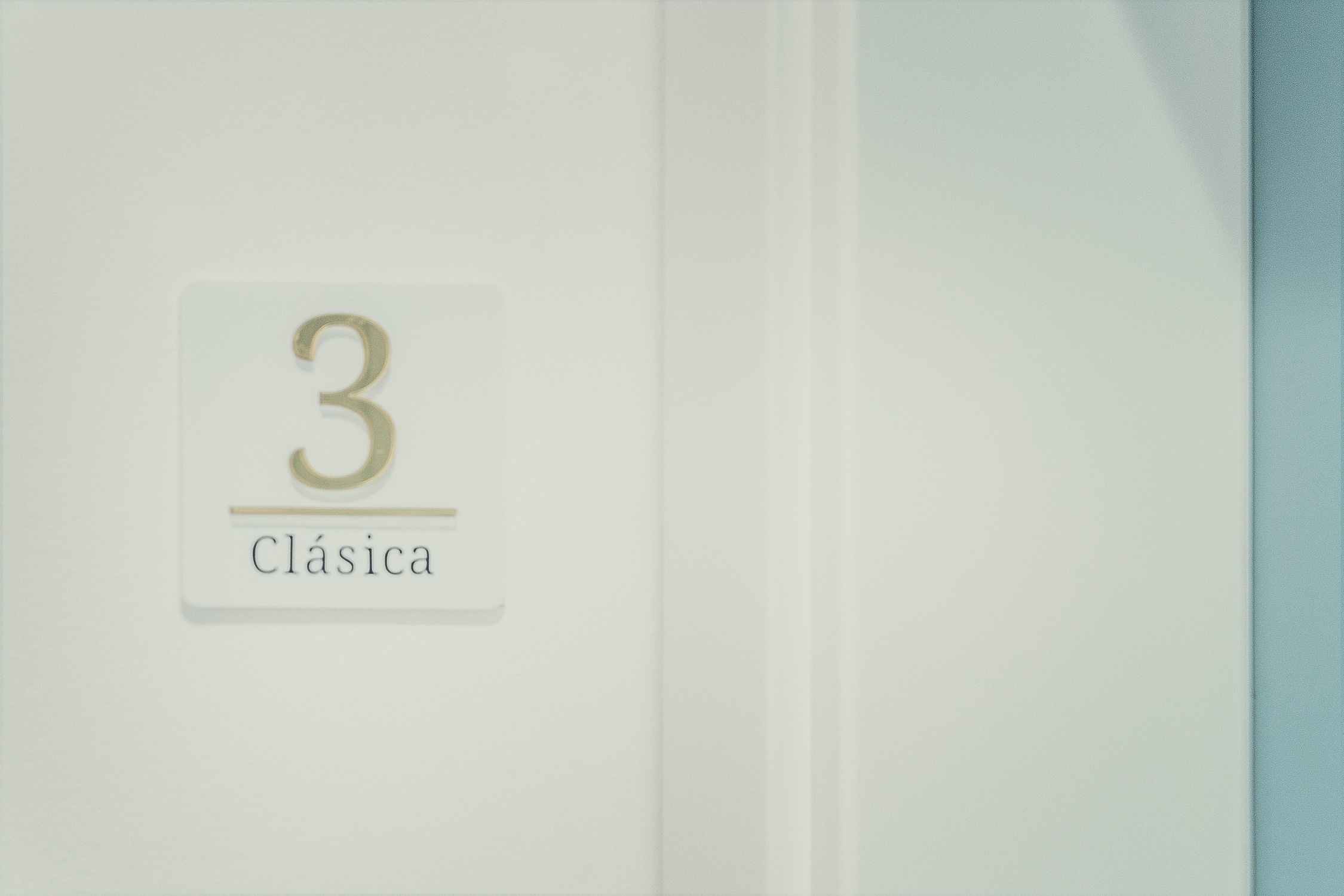 Un cartel blanco con el número "3" y la palabra "Clásica" está montado en una superficie clara, con un borde azul visible a la derecha.