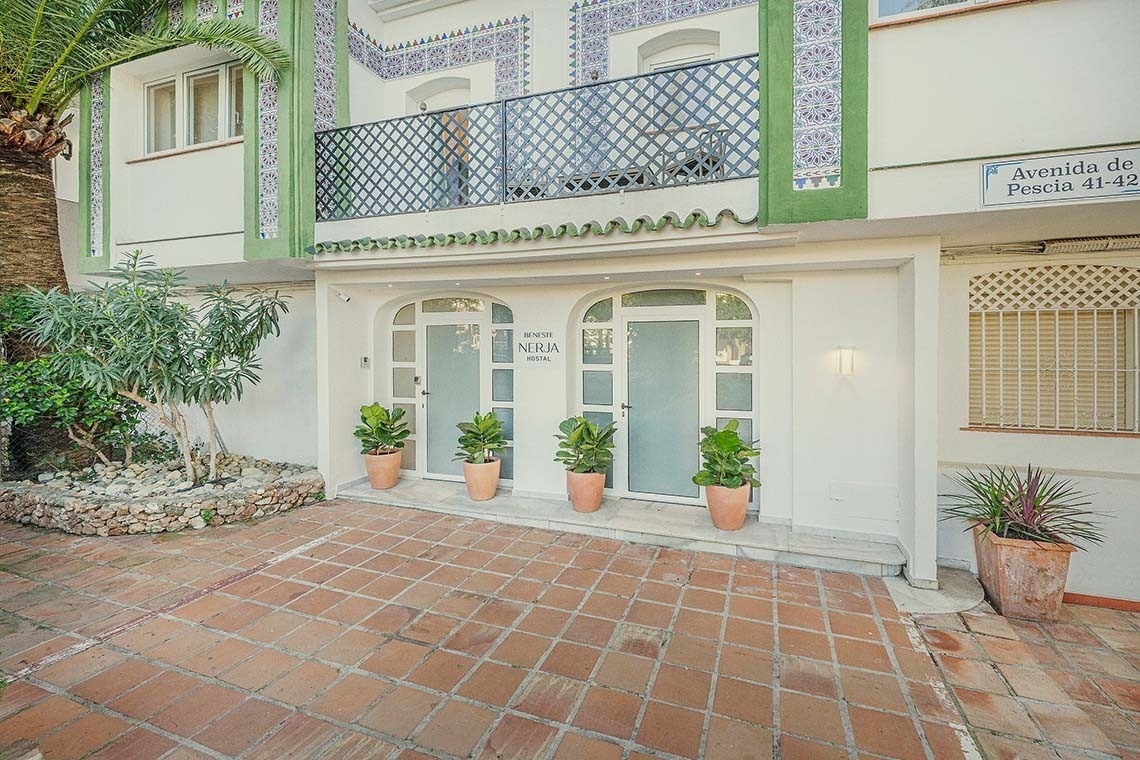 Fachada de Nerja Hostal | Beneste Hoteles | Web oficial. Puertas de entrada, macetas y balcón.