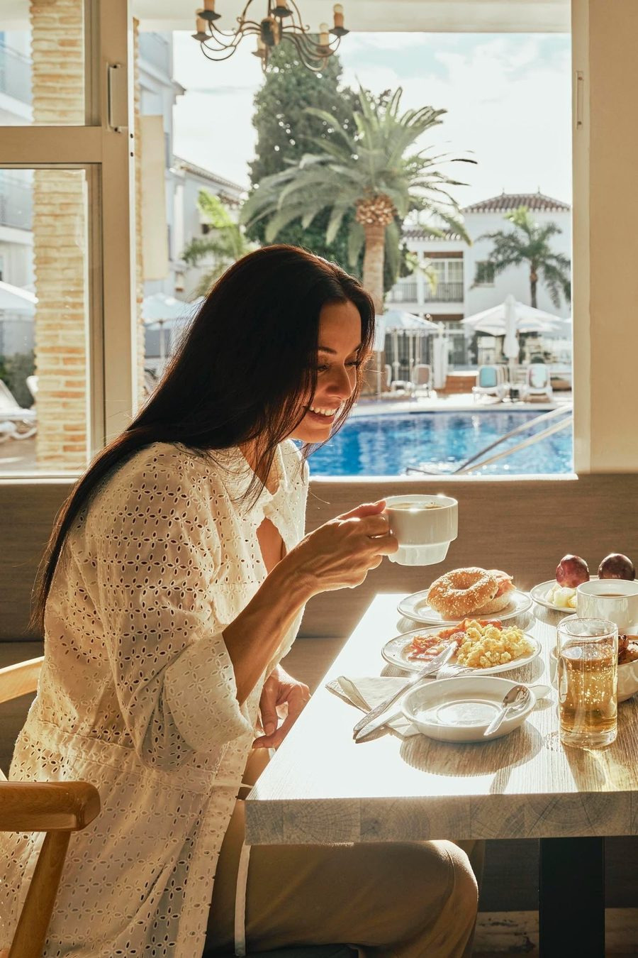 Mujer disfrutando desayuno con vistas a la piscina. BENESTE: Corporativa.
