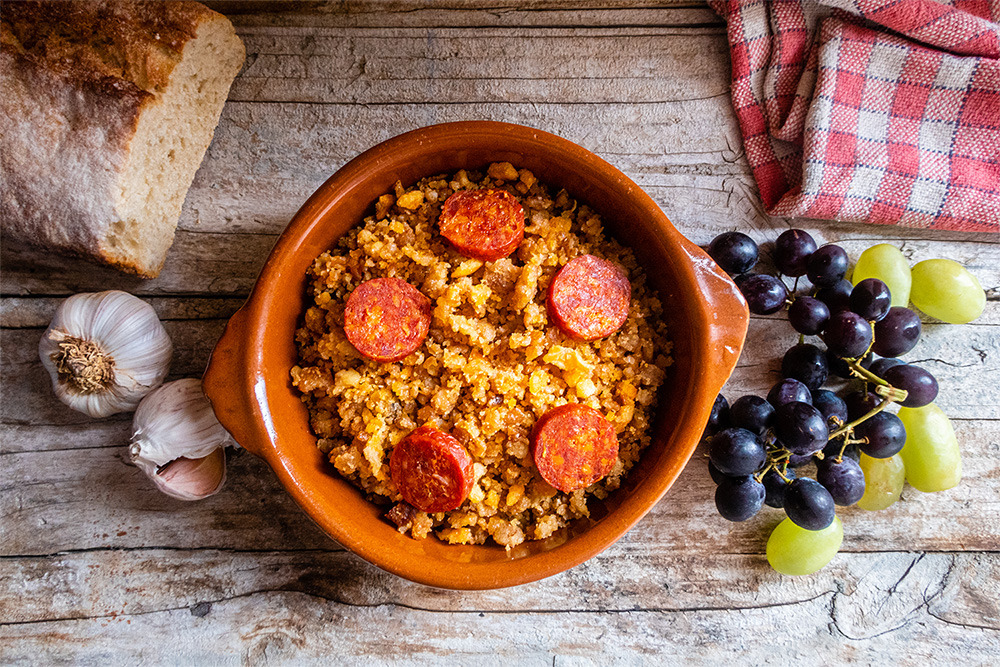 Plato de migas con chorizo, pan, ajos y uvas BENESTE: Corporativa en mesa rústica.