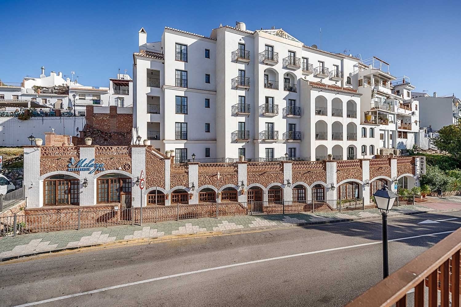Hotel Frigiliana | Beneste Hoteles: Fachada blanca con balcones y restaurante de ladrillo visto. ¡Reserva ya!