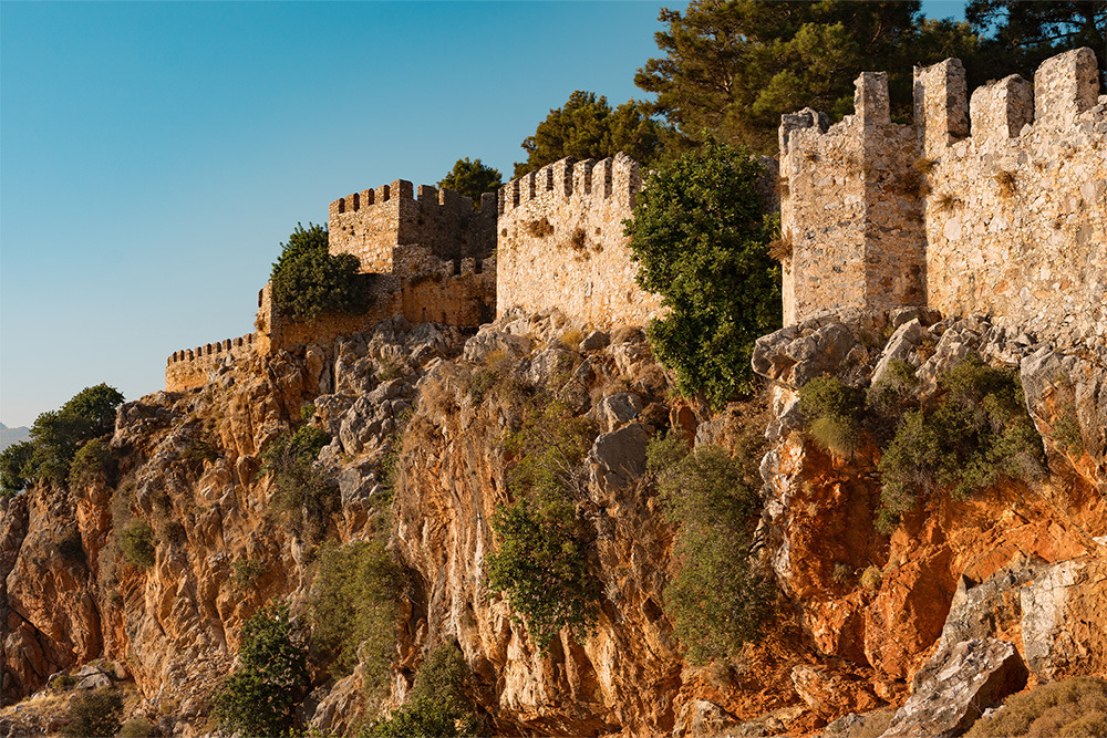 Castillo de Alanya BENESTE: Corporativa, murallas antiguas en acantilado rocoso bajo cielo azul.