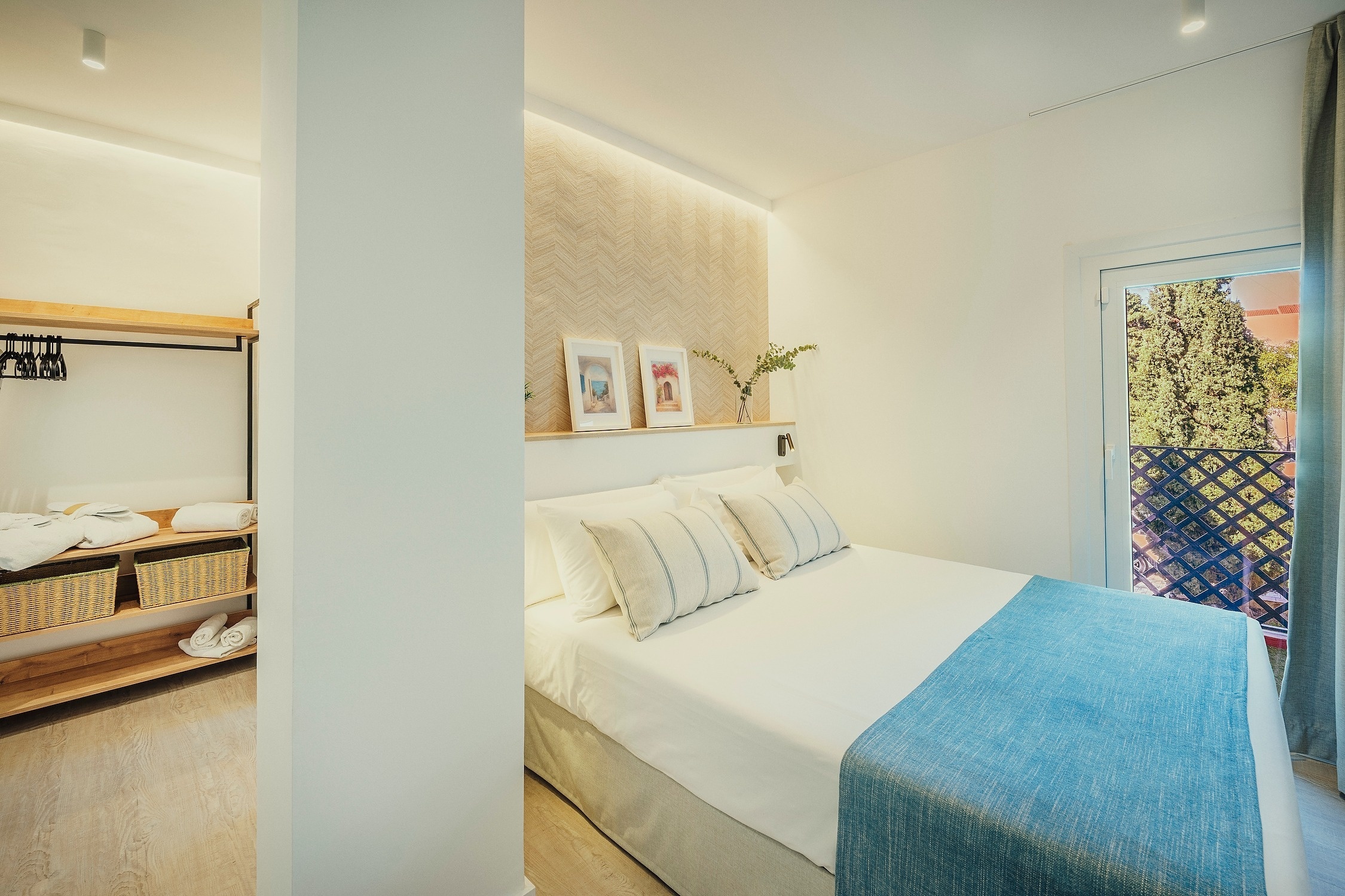 Una habitación moderna y luminosa con una cama grande, un cabecero decorado, un balcón con vistas a la naturaleza y un armario abierto con estantes de madera.