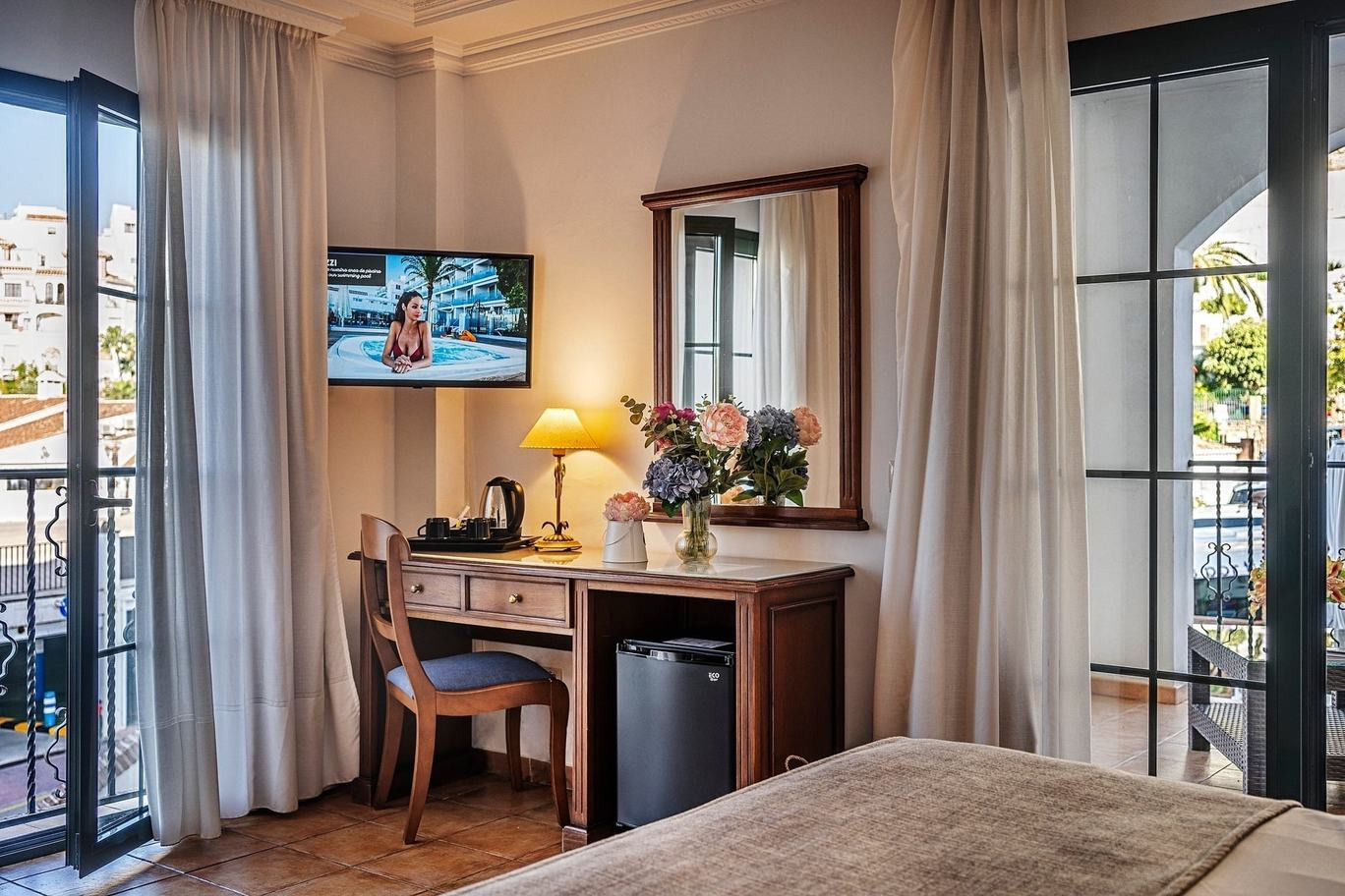 BENESTE: Corporativa. Habitación de hotel con escritorio, TV y balcón soleado.