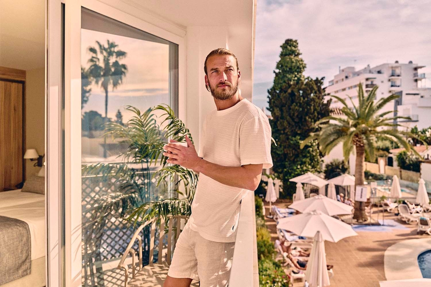Villa Flamenca | Beneste Hoteles: Hombre en balcón con café, vistas a piscina y palmeras.