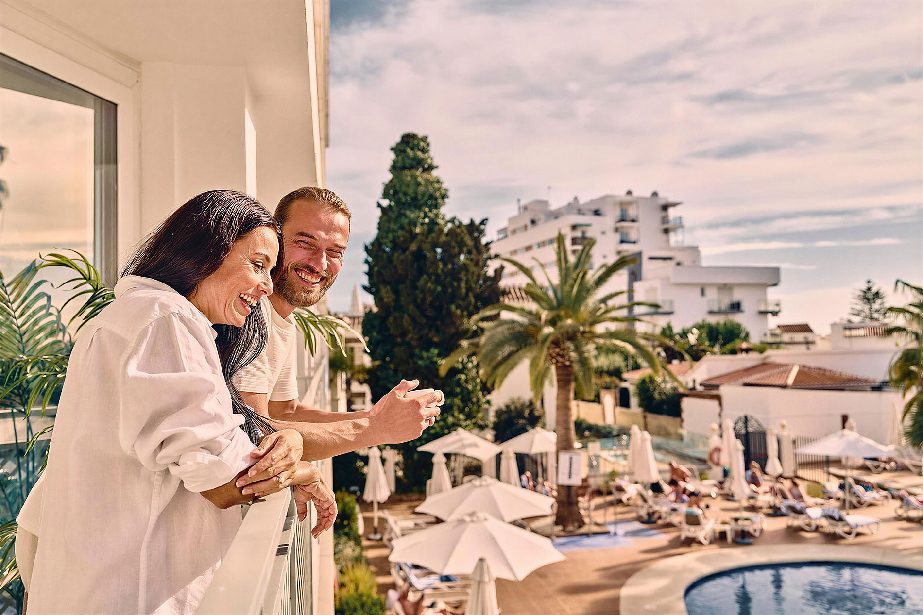 Couple enjoying a balcony view of a pool BENESTE: Corporativa resort.