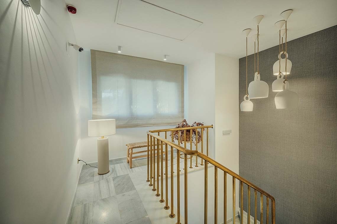 Pasillo moderno con lámpara de pie y barandilla dorada. Nerja Hostal | Beneste Hoteles | Web oficial.