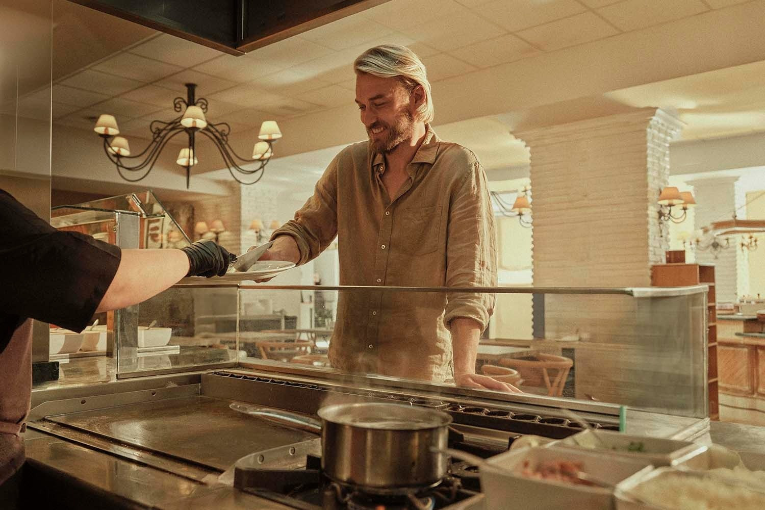Desayuno Buffet | Villa Flamenca | Beneste Hoteles | Web oficial: cliente sonriendo recibe plato en buffet.
