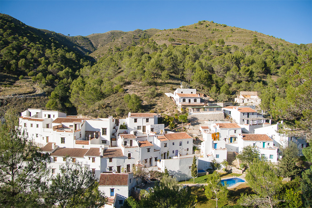 Pueblo blanco español conBENESTE: Corporativa, piscina y colinas boscosas.