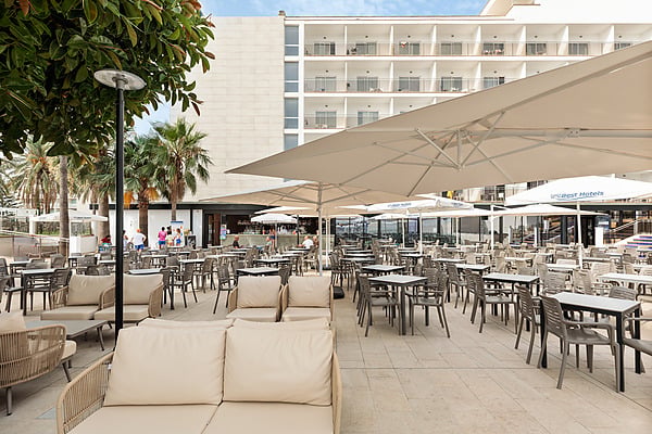 Terraza exterior con mesas y sillas frente a hotel blanco con balcones y vegetación frondosa. Hotel Best Siroco, Benalmádena | Best Hotels | Mejor Precio