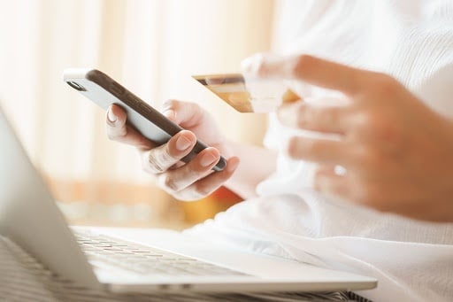 Eine Frau hält eine Kreditkarte und ein Handy in der Hand , während sie vor einem Laptop sitzt .