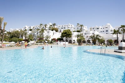 Piscina y hotelBest Corporativa con palmeras y tumbonas bajo un cielo despejado.