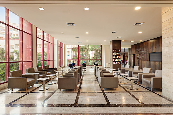 Lobby moderno del hotel con sofás rojos y mesas junto a una cascada y edificios verdes Hotel Best Jacaranda, Tenerife | Best Hotels | Mejor Precio