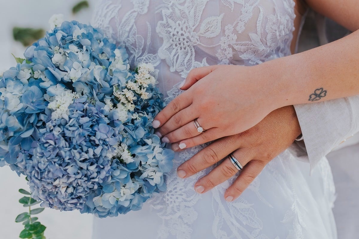 una novia sostiene un ramo de flores azules y blancas