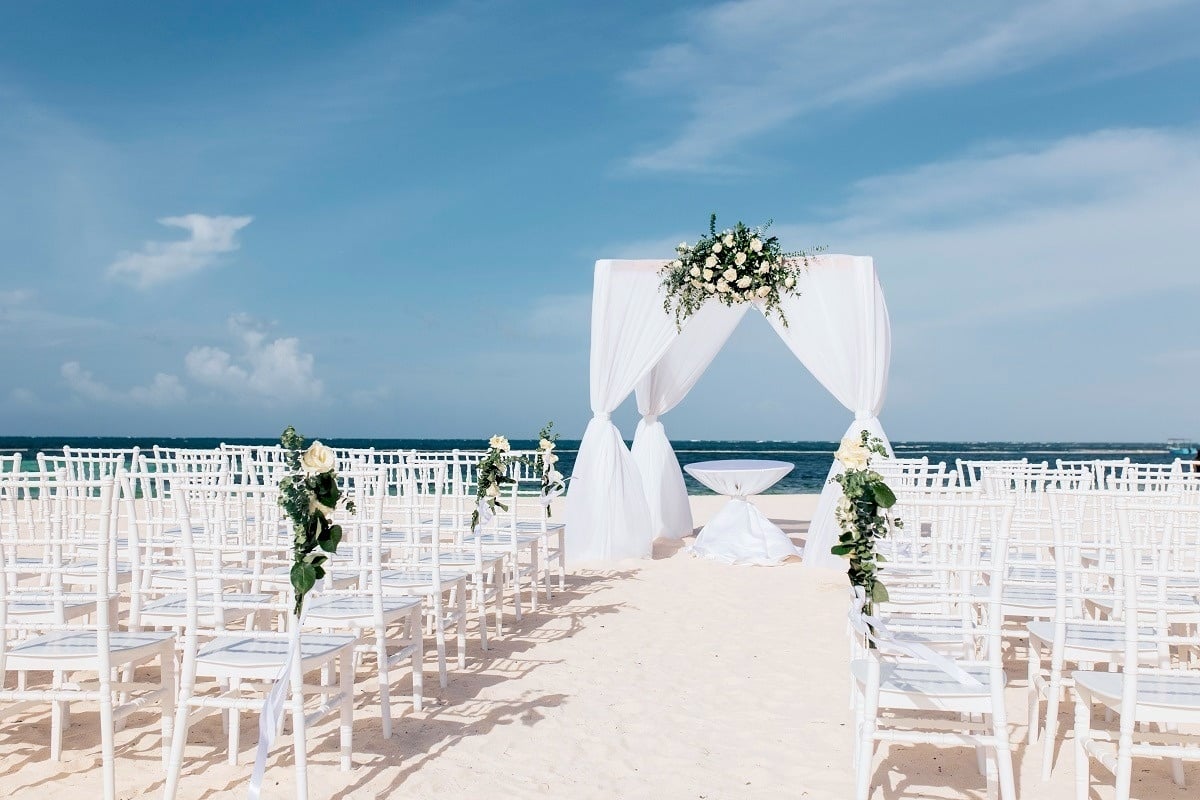 una boda en la playa con sillas blancas y un altar