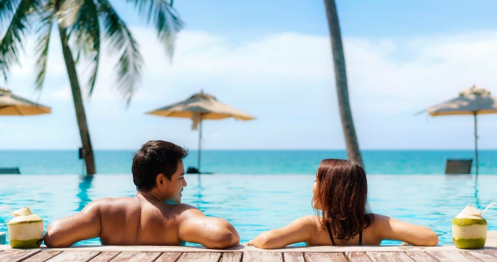 un homme et une femme se détendent dans une piscine avec des noix de coco à côté d' eux