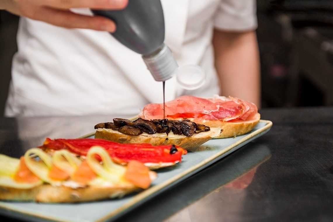 Eine Person gießt Essen auf einen Teller mit verschiedenen Speisen