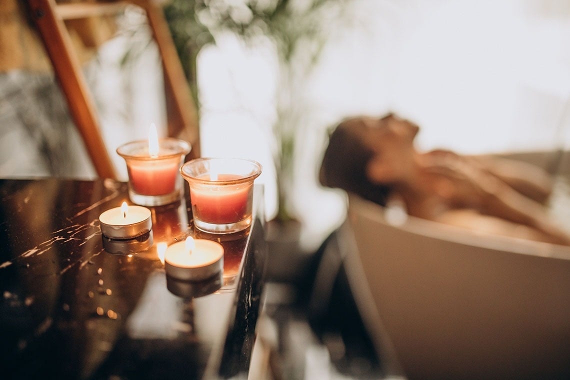 a woman laying in a bathtub with candles in front of her