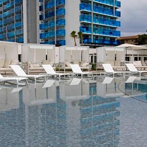 una piscina con sillas blancas y un edificio azul en el fondo