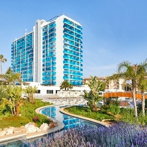 un gran edificio blanco con balcones azules está rodeado de palmeras y flores