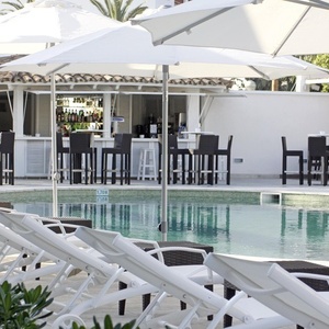 una piscina rodeada de sillas y sombrillas con un bar en el fondo