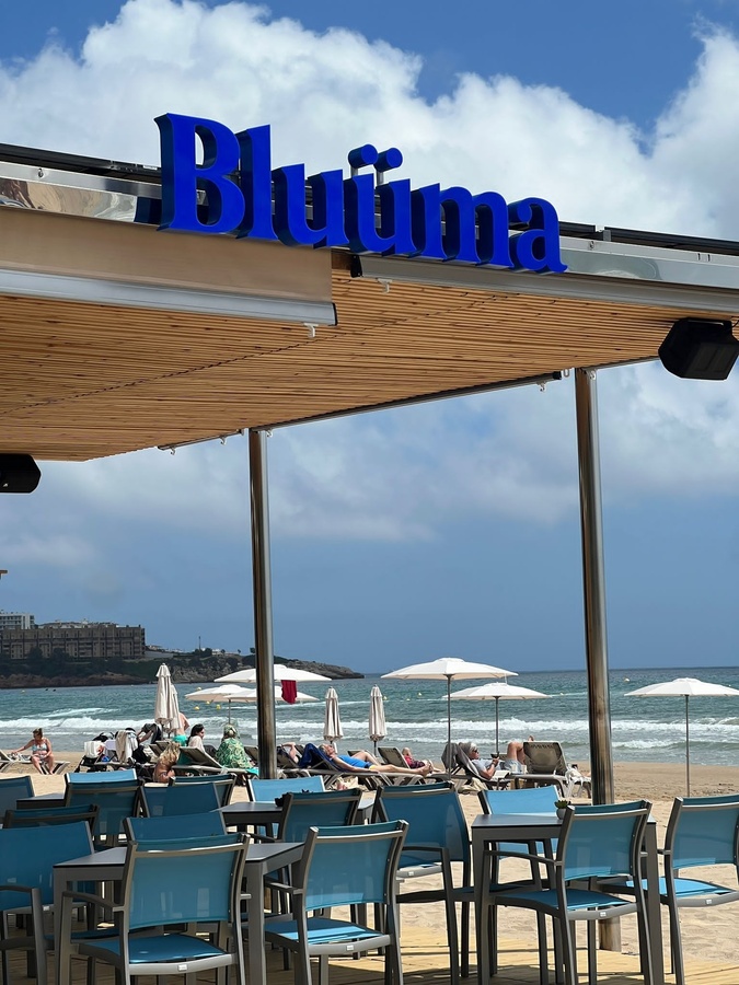 ein blaues Schild steht über einem Restaurant mit blauen Stühlen und Tischen am Strand