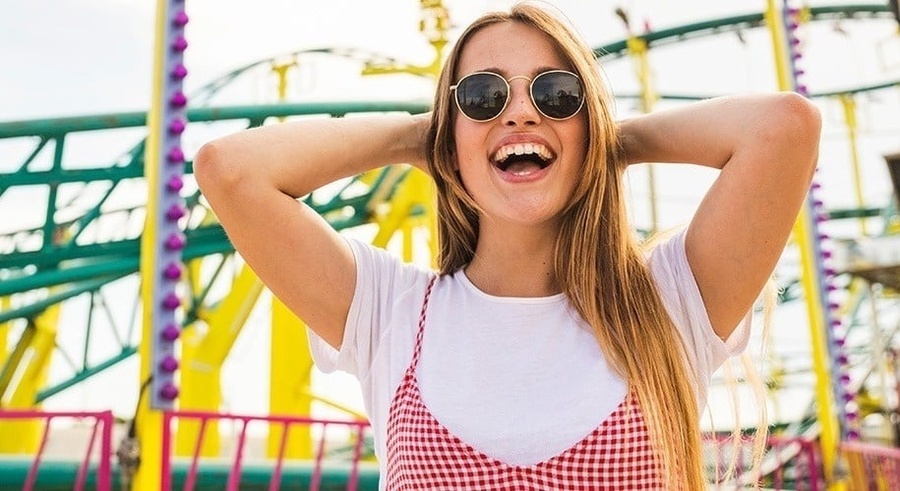 une femme portant des lunettes de soleil et un t-shirt blanc sourit avec ses mains derrière sa tête