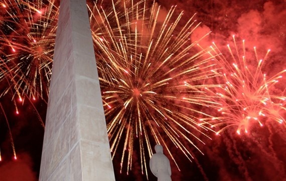 una estatua se encuentra frente a un obelisco mientras los fuegos artificiales explotan en el cielo