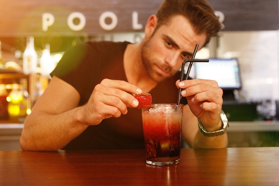 un hombre sostiene una fresa encima de un cóctel en un bar
