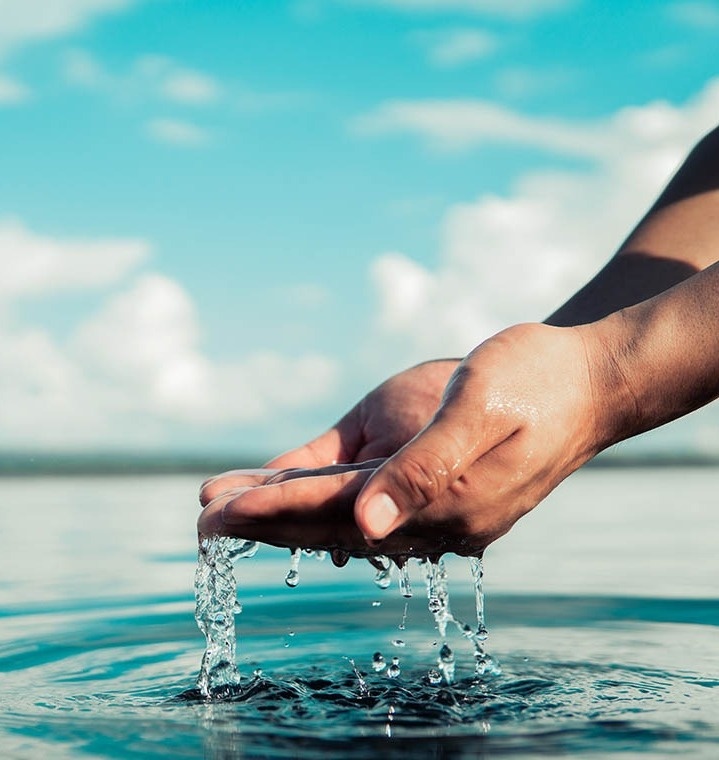 eine Person schöpft Wasser aus einem See mit ihren Händen