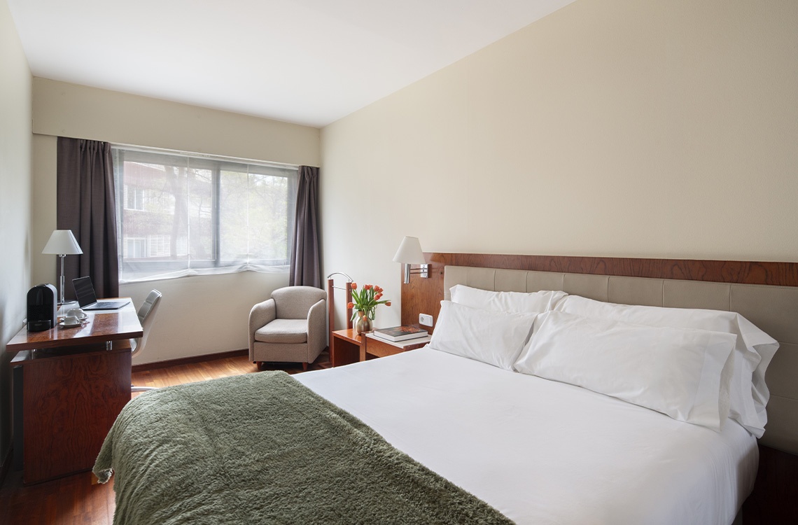 Comfortable hotel room with a plush bed, desk, and armchair, perfect for your Bohemian Hotels stay.
