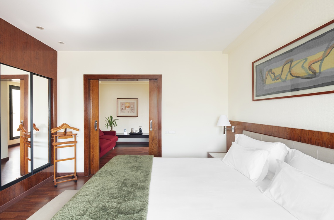 Elegant hotel room with a plush bed, mirrored closet, and a separate seating area, reflecting a bohemian hotel vibe.