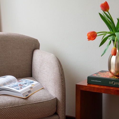 Cozy armchair with open book and orange tulips in a vase on a side table, perfect for Bohemian Hotels.