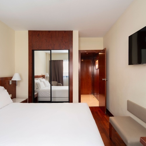 Elegant hotel room with a spacious bed, mirrored wardrobe, and a view into a hallway.