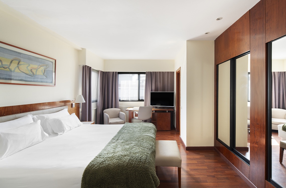 Modern hotel room with a king-size bed, desk, and mirrored closet doors.