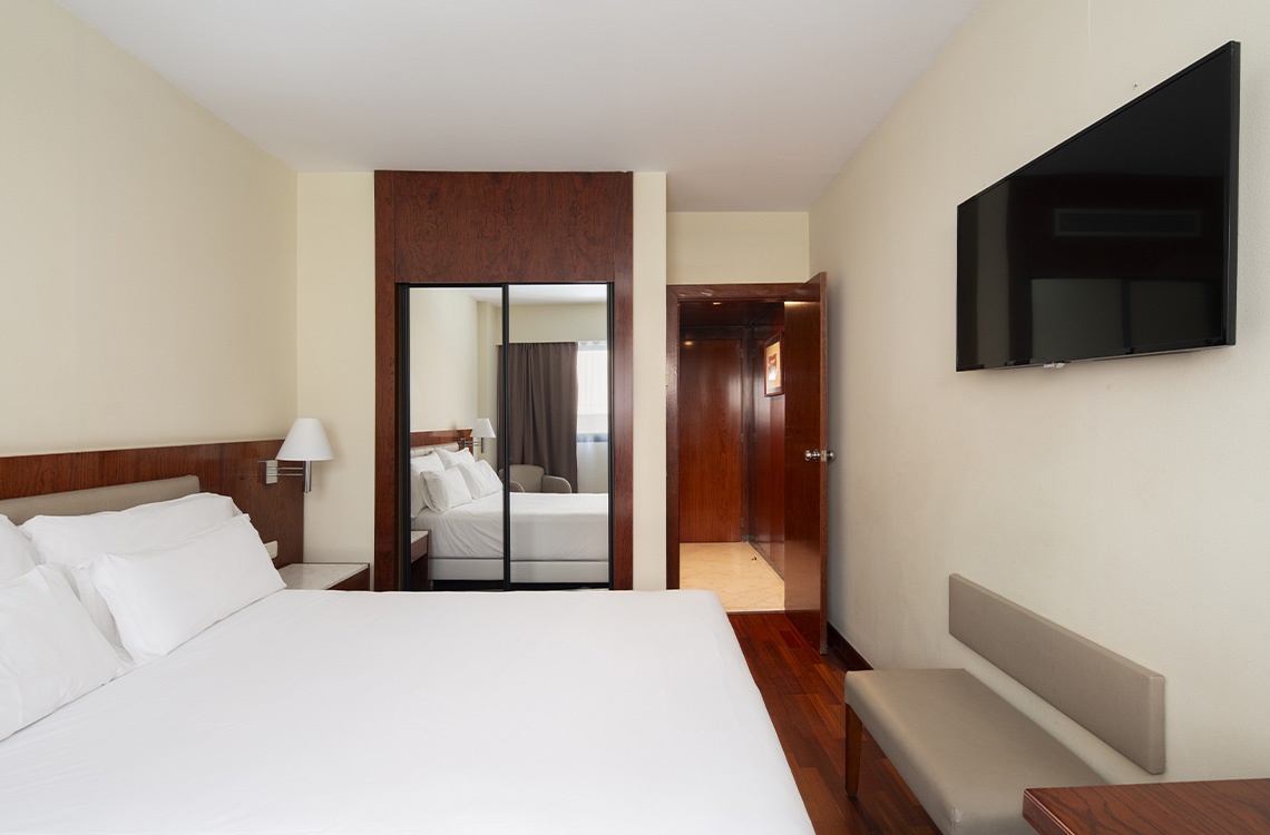 Spacious hotel room with a queen bed, mirror closet, and TV at Bohemian Hotels.