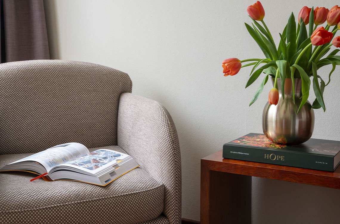 A comfortable armchair, open book, and tulip vase set a cozy scene in a Bohemian Hotels room.