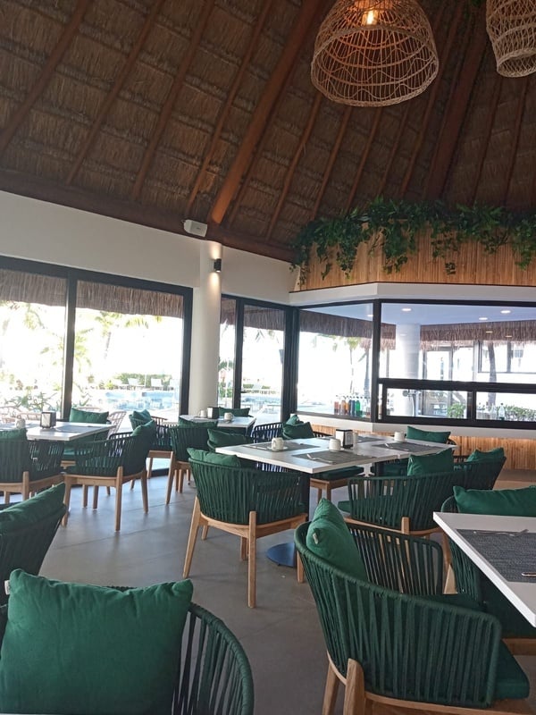 a restaurant with green chairs and tables and a thatched roof