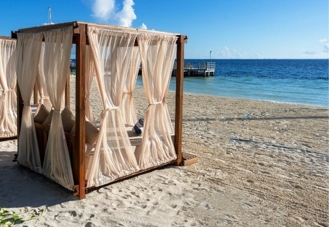 una cama con dosel en la playa con el océano al fondo